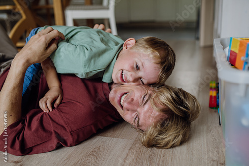 Portrait of father embracing his son at home, having fun, lying on floor and laughing. photo
