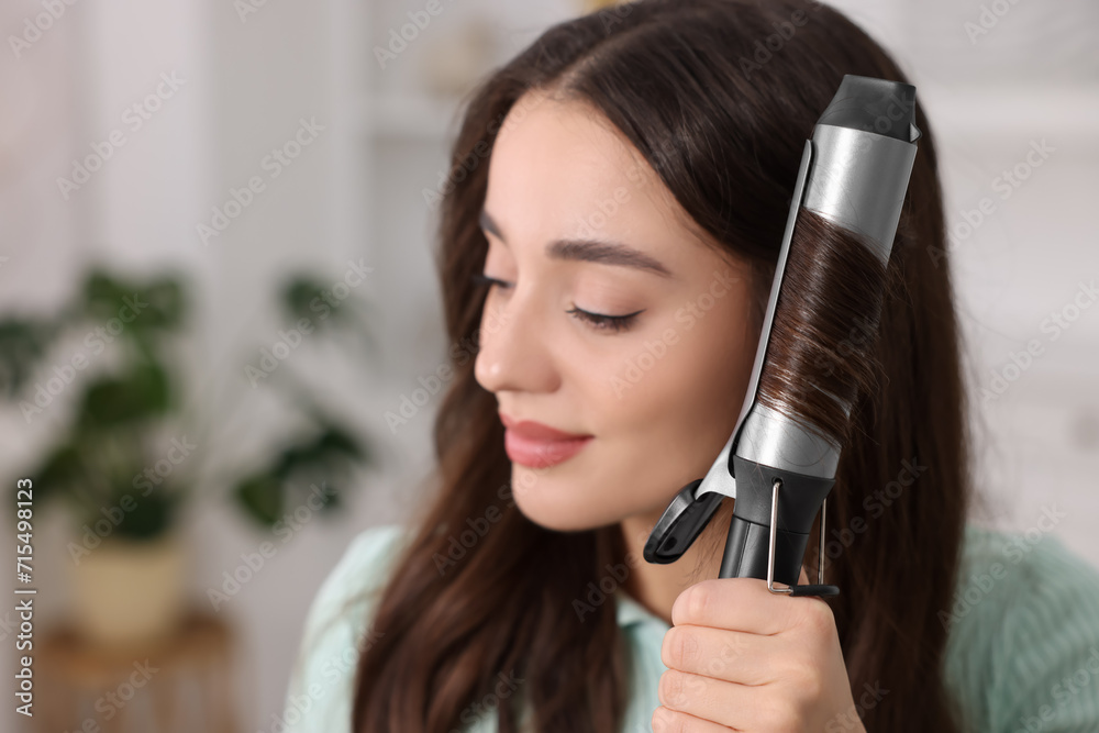Beautiful woman using curling hair iron indoors. Space for text Beautiful woman using curling hair iron indoors. Space for text