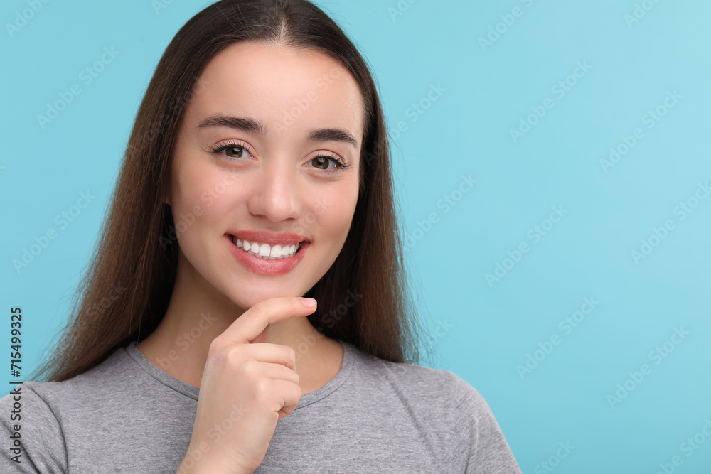 Young woman with clean teeth smiling on light blue background, space for text Young woman with clean teeth smiling on light blue background, space for text