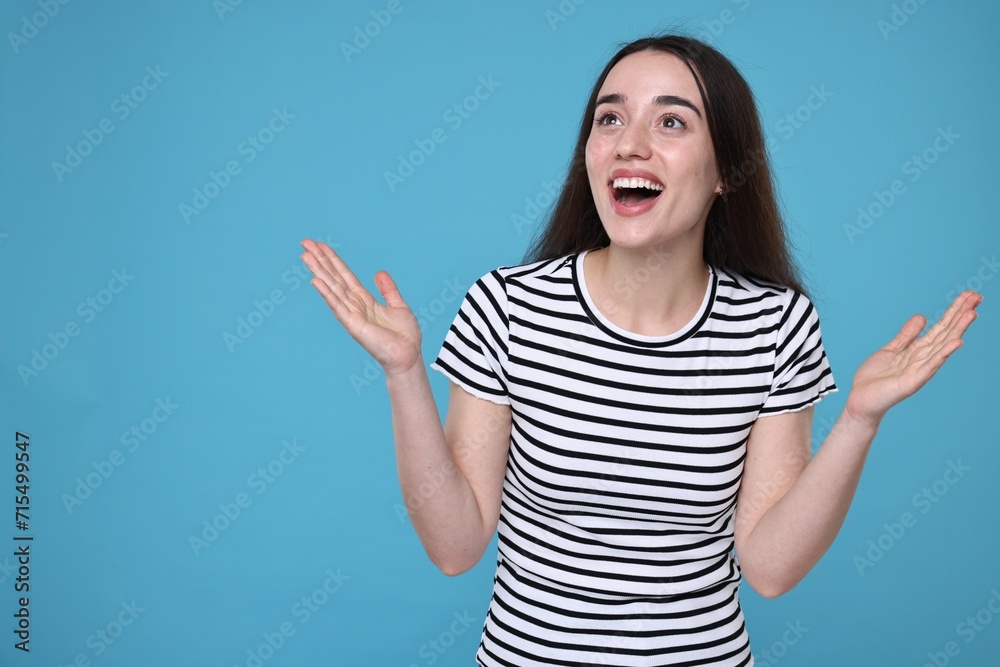 Portrait of happy surprised woman on light blue background. Space for text