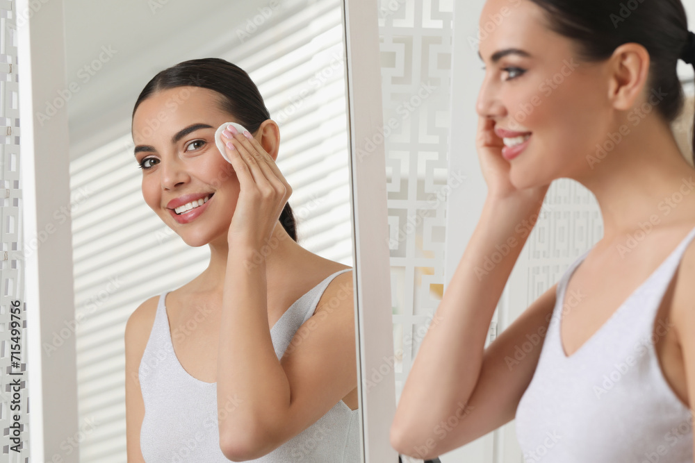 Beautiful woman removing makeup with cotton pad near mirror indoors Beautiful woman removing makeup with cotton pad near mirror indoors
