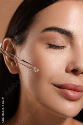 Beautiful young woman applying serum onto her face  closeup