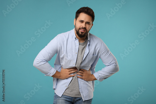Young man suffering from stomach pain on light blue background