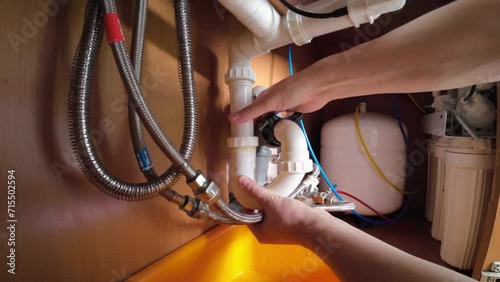 A man finishes assembling the plumbing and drainage system under the sink.