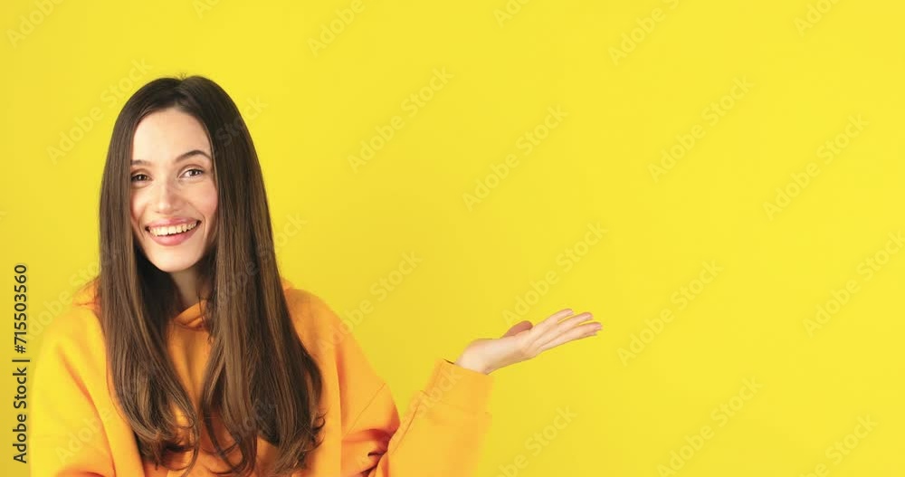 Excited surprised woman look at side, say wow and pointing index hands aside isolated on yellow background. Brunette girl in warm yellow hoody. Look over here. Sale here