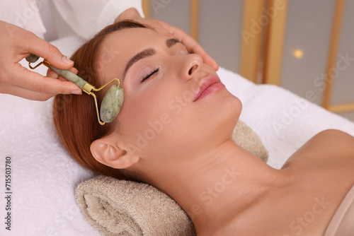 Young woman receiving facial massage with jade roller in beauty salon, closeup