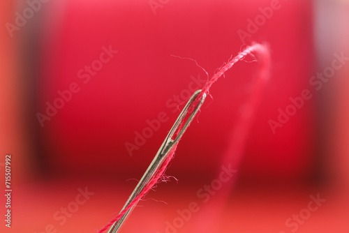 Close up of sewing needle on red thread spool blurred background.