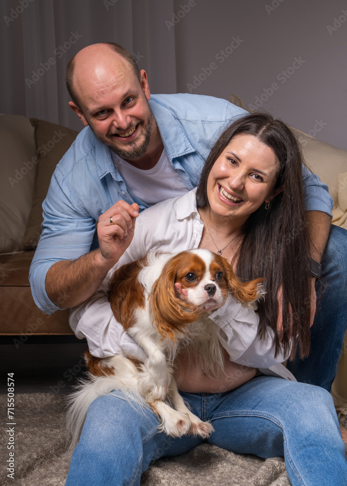 Happy family with a dog. A woman holds in her arms Cavalier King Charles Cocker Spaniel and laughs cheerfully, a man looks tenderly at the animal Happy family with a dog. A woman holds in her arms Cavalier King Charles Cocker Spaniel and laughs cheerfully, a man looks tenderly at the animal