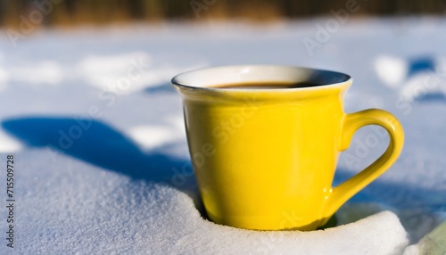 winter background yellow cup with hot coffee or tea stand on the snow outdoor at sunny day with cold weather outdoors