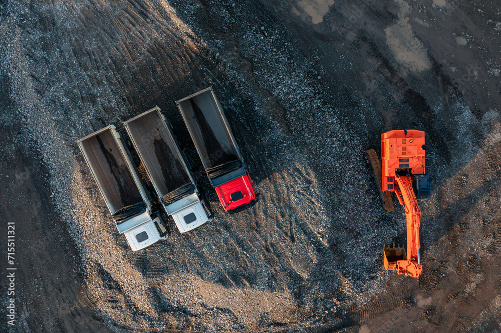 Aerial drone view of excavator and dump trucks in construction site by the sea side. Construction industry