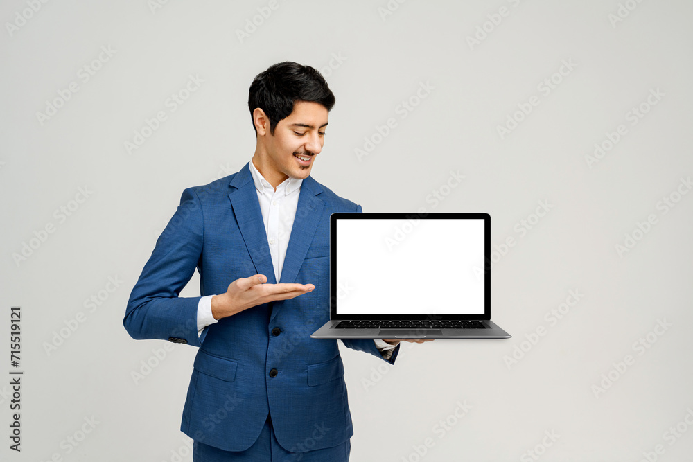 Hispanic businessman in a blue suit presents a laptop with a blank screen, providing a versatile image for showcasing software, websites, or any digital product