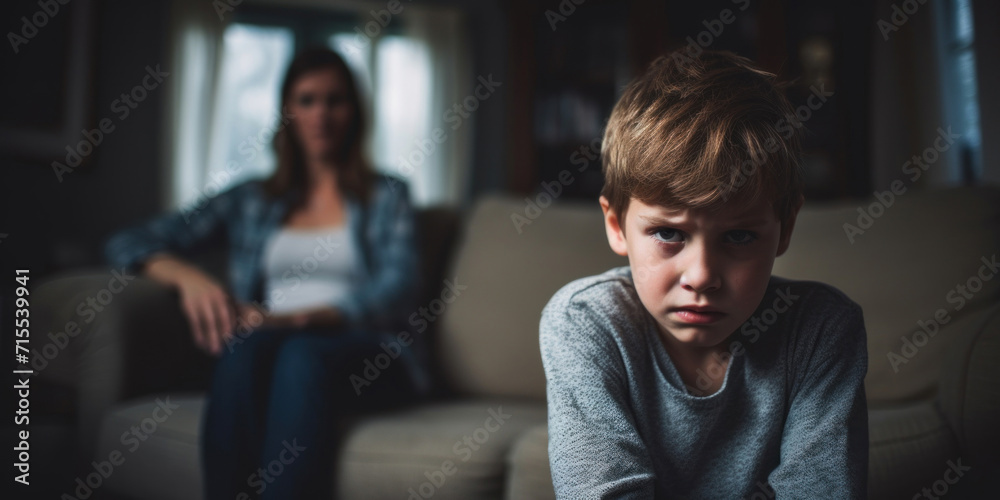 Fototapeta premium A portrait of a troubled young boy with a look of concern, with a blurred figure of a parent behind.