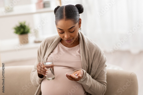 Healthy young pregnant black woman holding pill glass of water photo