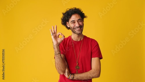 Happy man showing ok gesture looking at camera isolated on yellow background in studio photo