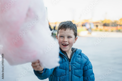 A cheerful young boy holding a large pink cotton candy in an outdoor setting