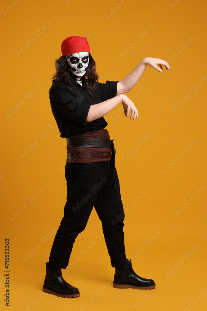 Fototapeta premium Man in scary pirate costume with skull makeup posing on orange background. Halloween celebration