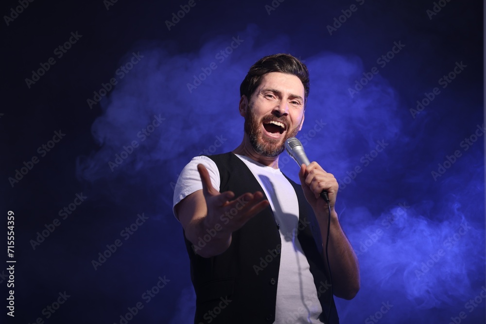 Handsome man with microphone singing on dark blue background Handsome man with microphone singing on dark blue background