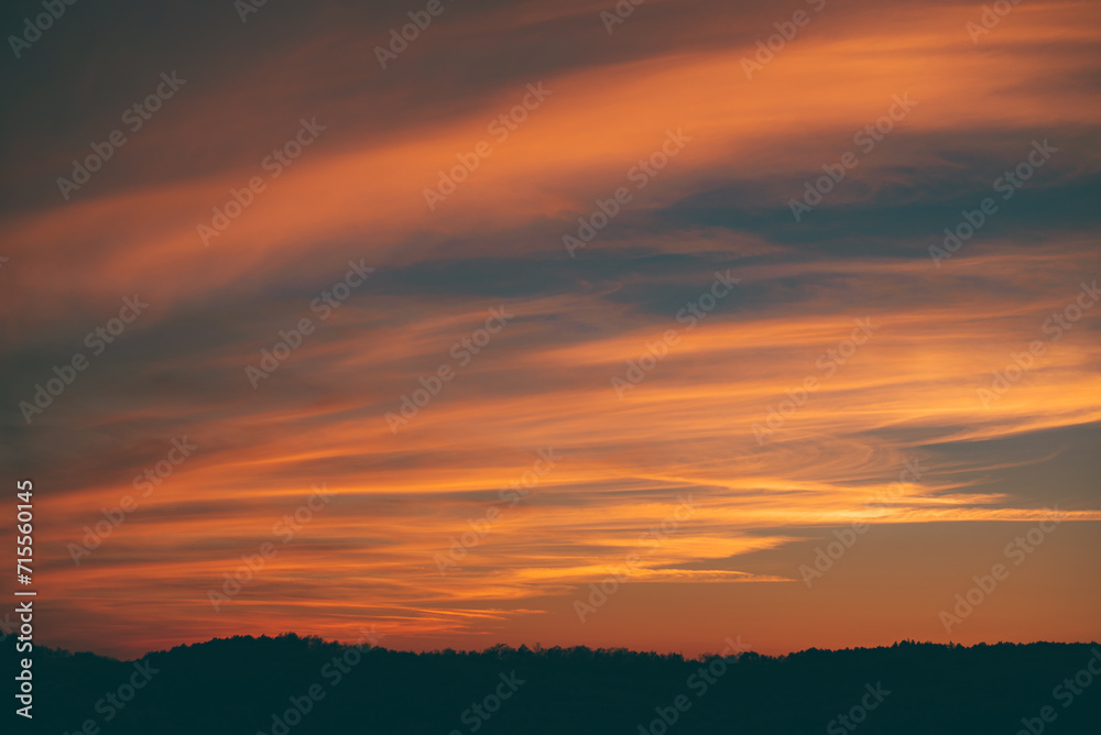 Vibrant sunset seen from the wild forest. Pastel colors in the evening sky. Cloud formations in abstract shapes