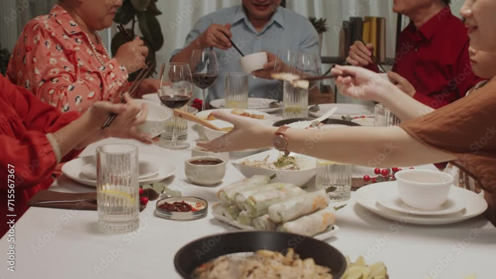 Handheld shot of big multi-generational Asian family having dinner at festive table using chopsticks Handheld shot of big multi-generational Asian family having dinner at festive table using chopsticks