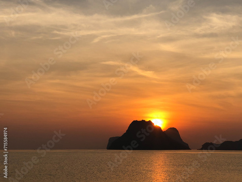 Vivid Orange Sunset Over Rocky Ocean Shoreline with Silhouetted Beach and Cloudy Sky on a Summer Evening