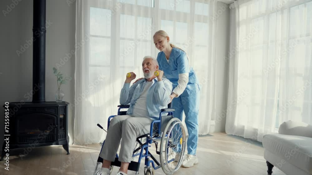 Nurse woman cares old man in wheelchair. Paralyzed elderly man does exercises with effort under supervision of nurse supporting. Living with spine legs paralysis, special needs people health concept. Nurse woman cares old man in wheelchair. Paralyzed elderly man does exercises with effort under supervision of nurse supporting. Living with spine legs paralysis, special needs people health concept.