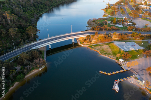 Aerial view of a curved road bridge over a river joining a forest area and a coastal town