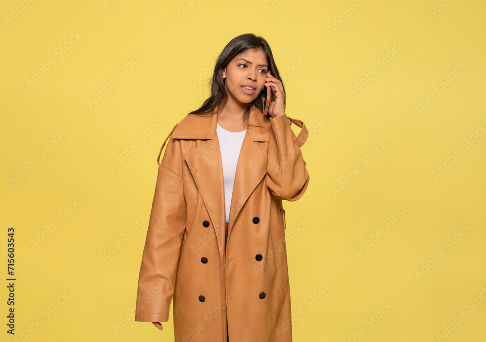 woman in jeans, a white t-shirt, and a brown coat using a mobile phone sitting on a yellow background. Happy people woman in jeans, a white t-shirt, and a brown coat using a mobile phone sitting on a yellow background. Happy people