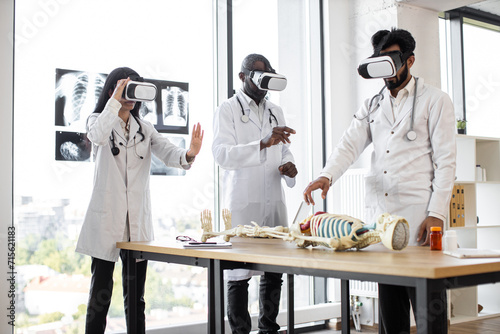 Human anatomy, VR, education, medicine concept. Young multiracial researchers using virtual reality goggles while working with human skeleton. Team of scientists in modern laboratory