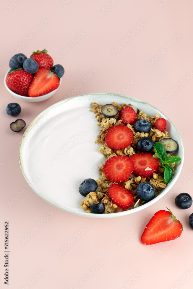 Yogurt bowl with granola and fresh berries: strawberries and blueberries on a pink background. Yogurt bowl with granola and fresh berries: strawberries and blueberries on a pink background.