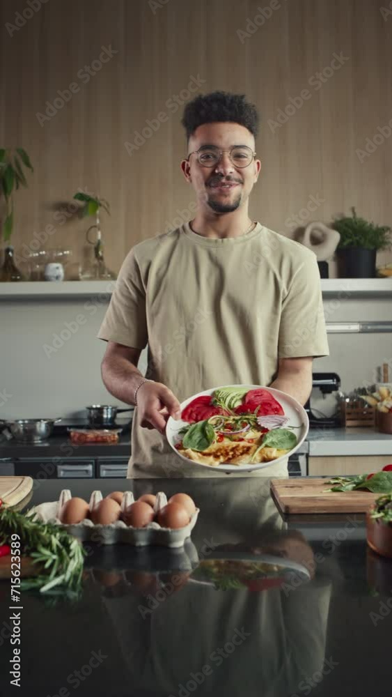 Vertical shot of food blogger adding fresh herbs to omelet, talking and showing dish on camera while giving online cooking class of filming culinary show