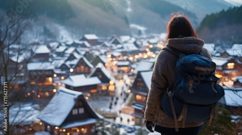 Young woman traveler looking at the beautiful UNESCO heritage village in the snow in winter at Shirakawa-go, Japan in twilight time.