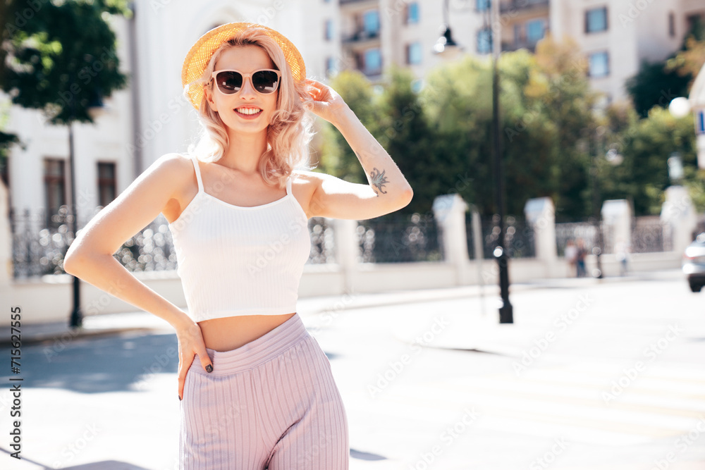 Young beautiful smiling blond hipster woman in trendy summer clothes. Carefree female posing in the street at sunny day. Positive model outdoors at sunset. Cheerful and happy in hat, sunglasses Young beautiful smiling blond hipster woman in trendy summer clothes. Carefree female posing in the street at sunny day. Positive model outdoors at sunset. Cheerful and happy in hat, sunglasses