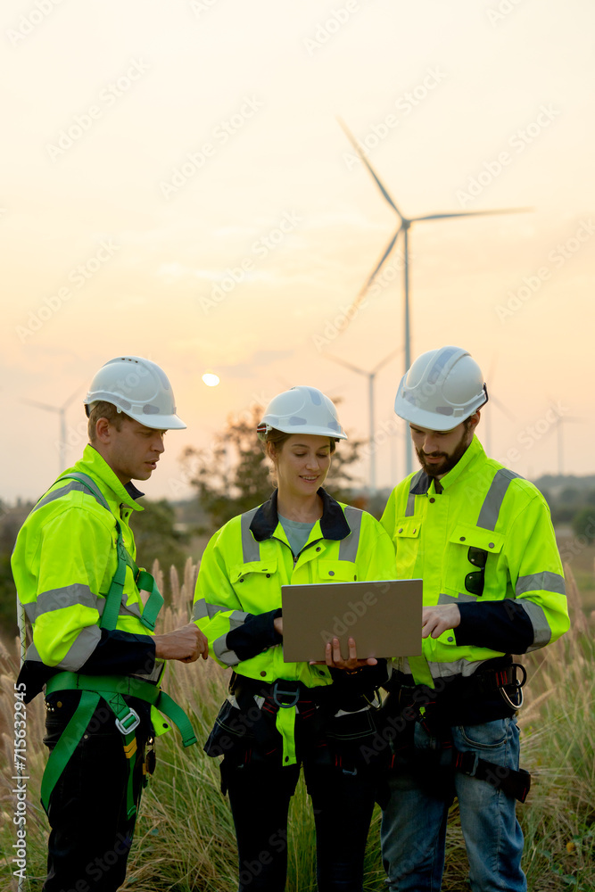 Vertical image group of technician workers man and woman work using laptop and stay in front of windmill or wind turbine with evening light. Vertical image group of technician workers man and woman work using laptop and stay in front of windmill or wind turbine with evening light.