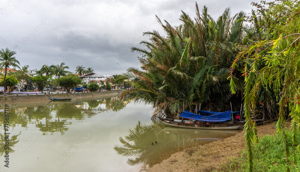 Obraz premium Traditional Vietnamese boat gracefully navigates the tranquil river, surrounded by lush, vibrant nature.