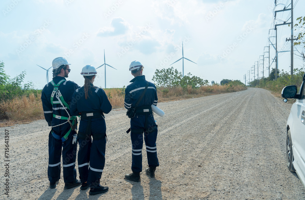 Back of group of technician workers stand on the road and discuss about work with windmill or wind turbine on the background.