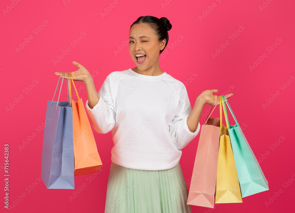 Cheerful young asian lady holding colorful shopping bags and winking