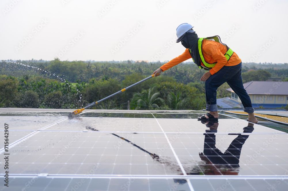 Professional worker cleans solar panels with brush and rinses with water on roof structure of construction factory. Technician uses a mop to clean dirt and dust, green electric power technology Professional worker cleans solar panels with brush and rinses with water on roof structure of construction factory. Technician uses a mop to clean dirt and dust, green electric power technology