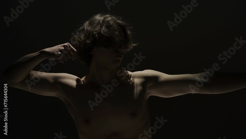 Portrait of male model in studio on the black background under spotlight. Attractive man silhouette imitating archery bow at the camera.