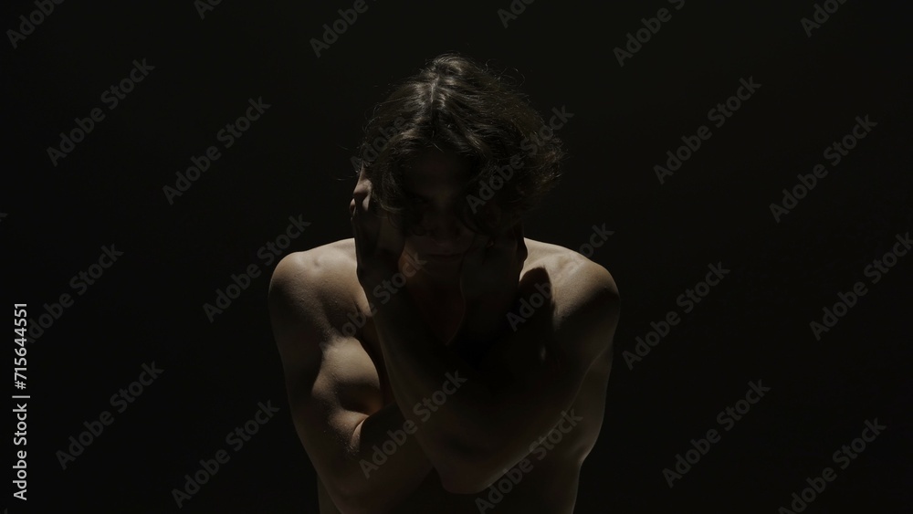 Portrait of male model in studio on the black background under spotlight. Attractive man silhouette looks down at the camera. Portrait of male model in studio on the black background under spotlight. Attractive man silhouette looks down at the camera.