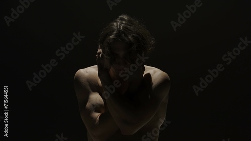 Portrait of male model in studio on the black background under spotlight. Attractive man silhouette looks down at the camera.