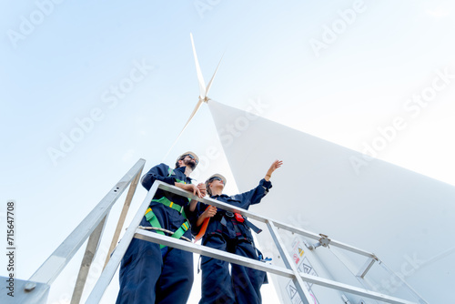 Lower view of professional technician man and woman stay on base of windmill or wind turbine and woman also point to the right with blue sky.
