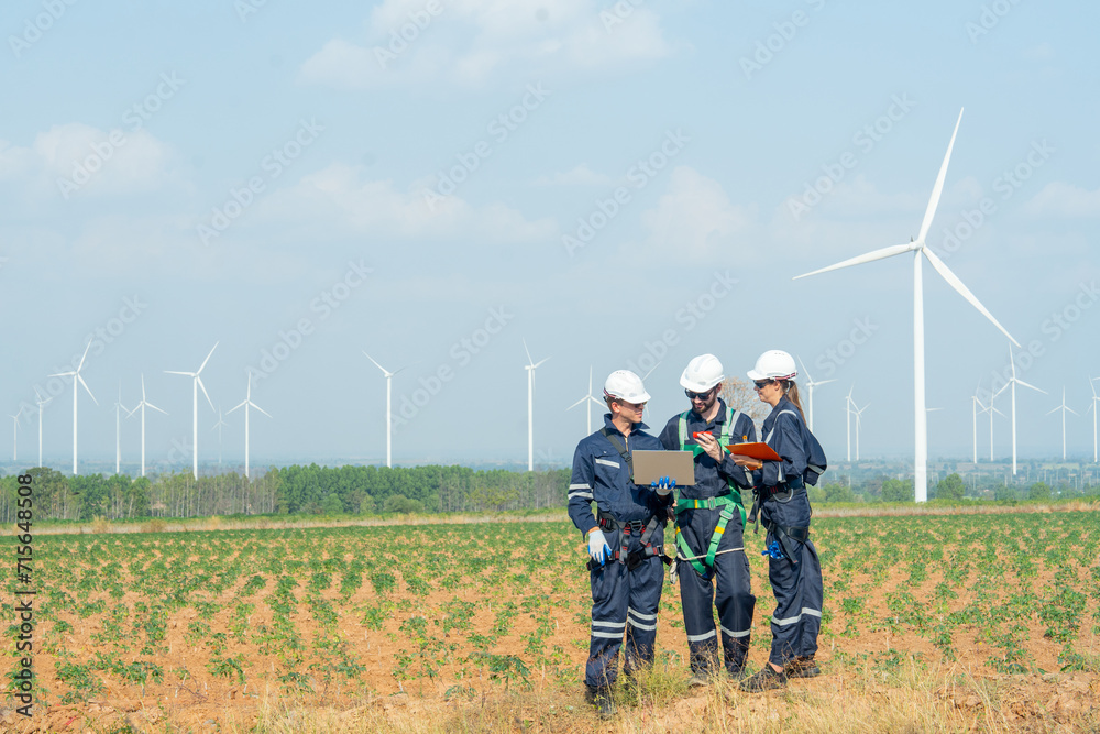Side view technician workers man and woman stand in front of row of windmill or wind turbine and work together using laptop with day light. Side view technician workers man and woman stand in front of row of windmill or wind turbine and work together using laptop with day light.
