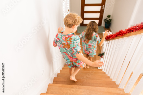 siblings in matching Christmas pyjamas racing downstairs photo