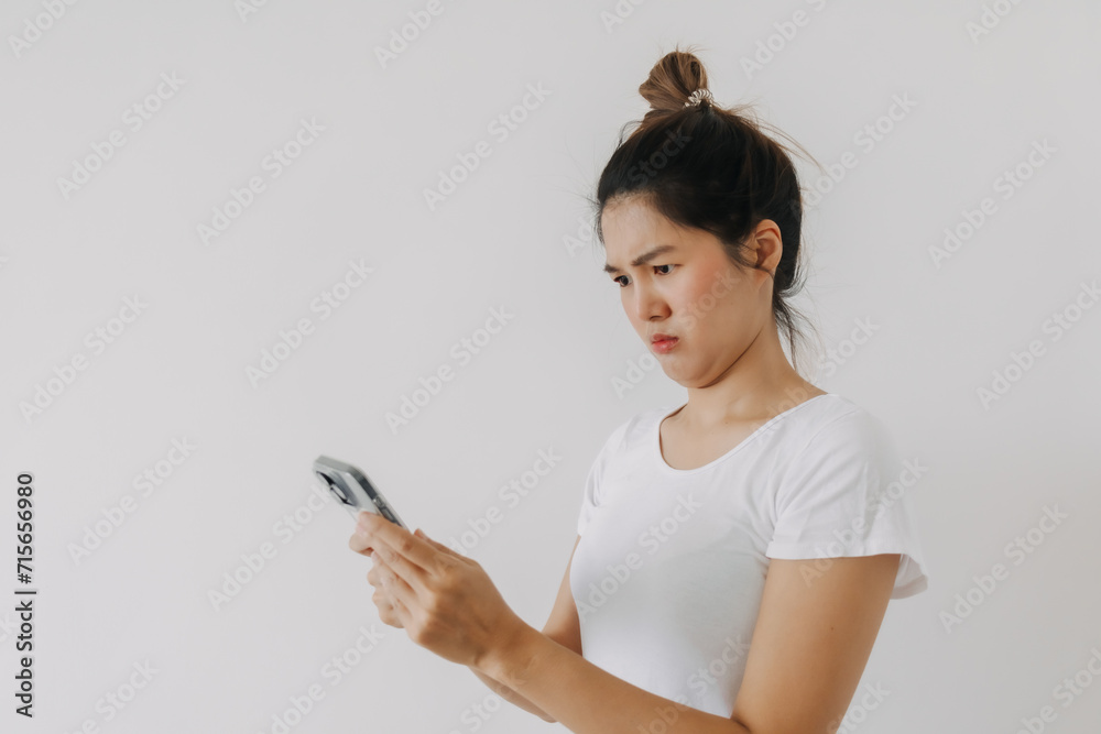 Asian Thai woman using mobile phone and looking with funny doubt face, holding smartphone by silent suspicious, standing isolated over white background wall. Asian Thai woman using mobile phone and looking with funny doubt face, holding smartphone by silent suspicious, standing isolated over white background wall.
