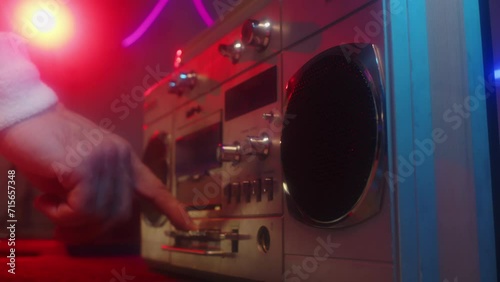 Close up of hand of unrecognizable person loading cassette into boombox preparing for party or fitness class in studio with neon lights photo