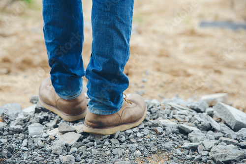 Legs of Lonely man wearing jeans and leather boots walking along the path strewn with rocks. Travel Concept.