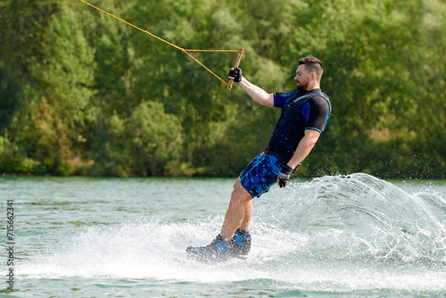 a male wakeboarder without a helmet rides on the water and holds on to the winch with one hand