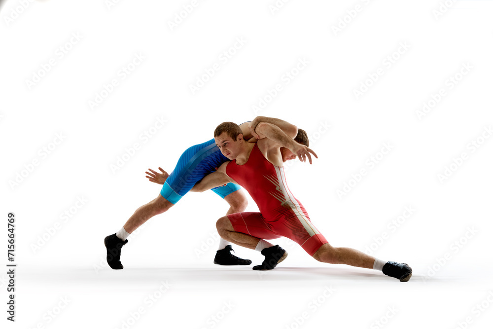 Two strong and skilled wrestlers in blue and red wrestling uniform are wrestling and doing grapple against white studio background. Concept of fair wrestling, championship, win competition.