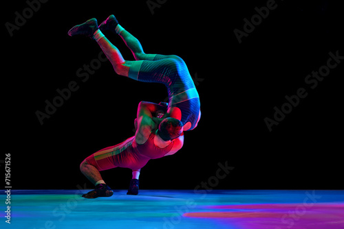 Fototapeta Naklejka Na Ścianę i Meble -  Two young man, professional sportsman of freestyle wrestling in uniform fighting against black background in mixed neon lights. Concept of motion, action, combat sports, strength and power, movement.