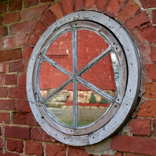 Reflection of red old mill in round window: square photo, red brick.